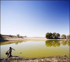 A boy steps gingerly through the mud after scooping water to use for bathing at his home in a nearby village. 